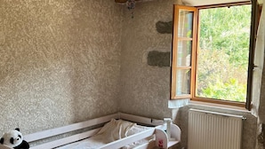 Um quarto pequeno e rústico com uma cama de solteiro, um candeeiro pendente, uma janela com vista para o verde e um radiador.