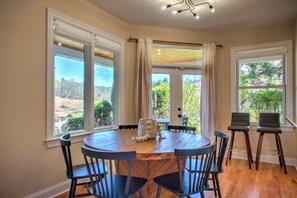 A dining area with a round table, chairs, and a view of a landscape through large windows.