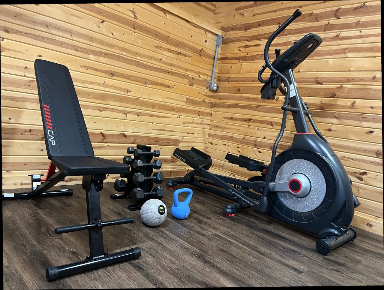 Een sportschool thuis met een hometrainer, een bankje, gewichten, een kettlebell en een medicine ball.