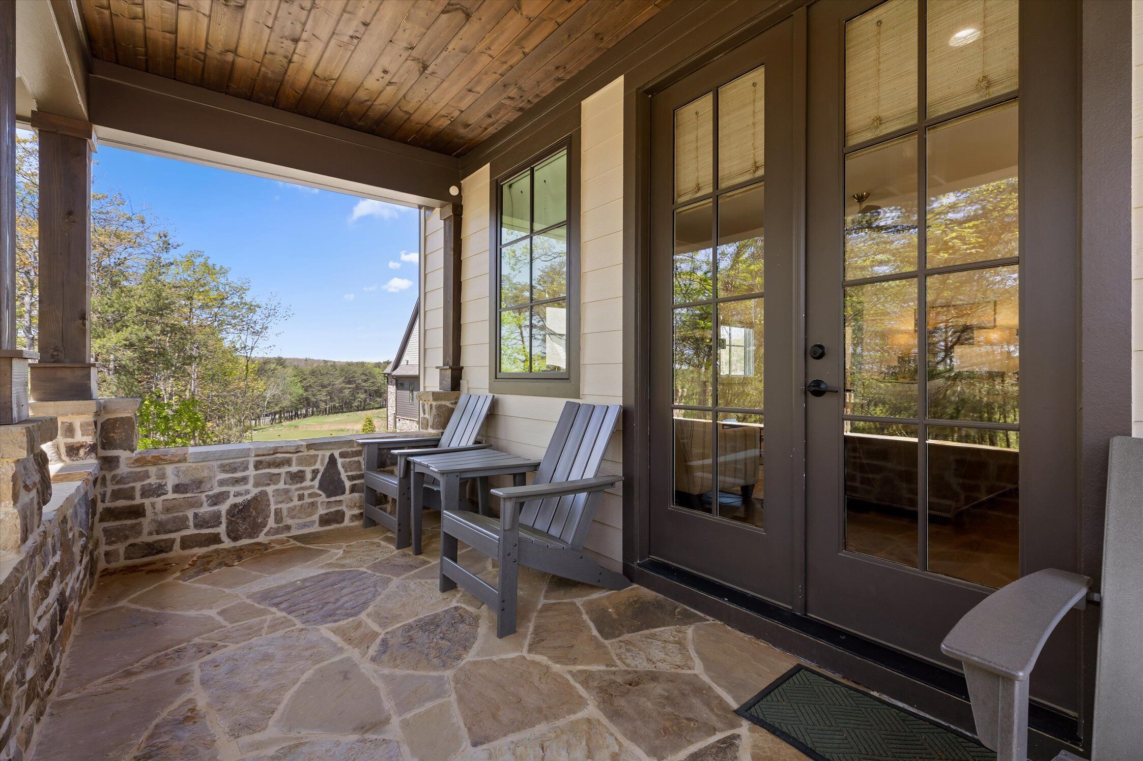 Eine überdachte Terrasse mit Steinboden, zwei Adirondack-Stühlen und einer Steinwand.