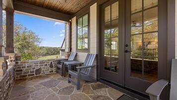 Eine überdachte Terrasse mit Steinboden, zwei Adirondack-Stühlen und einer Steinwand.