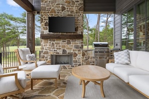 An outdoor patio with stone walls, a flat-screen TV, a grill, and a seating area with sofas and chairs. - McLemore Resort - 21 Peregrine Lane - Golf Course View (Rising Fawn)