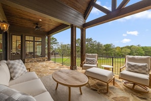 A covered outdoor seating area with stone flooring, wooden furniture, and a view of a green landscape. - McLemore Resort - 21 Peregrine Lane - Golf Course View (Rising Fawn)
