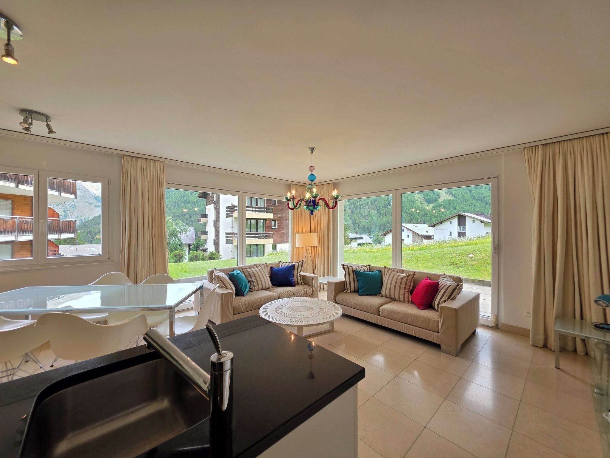 A spacious living room with a large window, a dining area, and a kitchen with a central island.