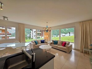 A spacious living room with a large window, a dining area, and a kitchen with a central island.