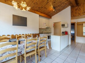 A dining area with wooden chairs and a table set for four, a kitchen with white cabinets and a microwave, and a wooden ceiling with exposed beams.