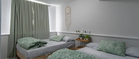 Un dormitorio con dos camas, una mesita de noche con una planta, un atrapasueños en la pared y una ventana con cortinas.