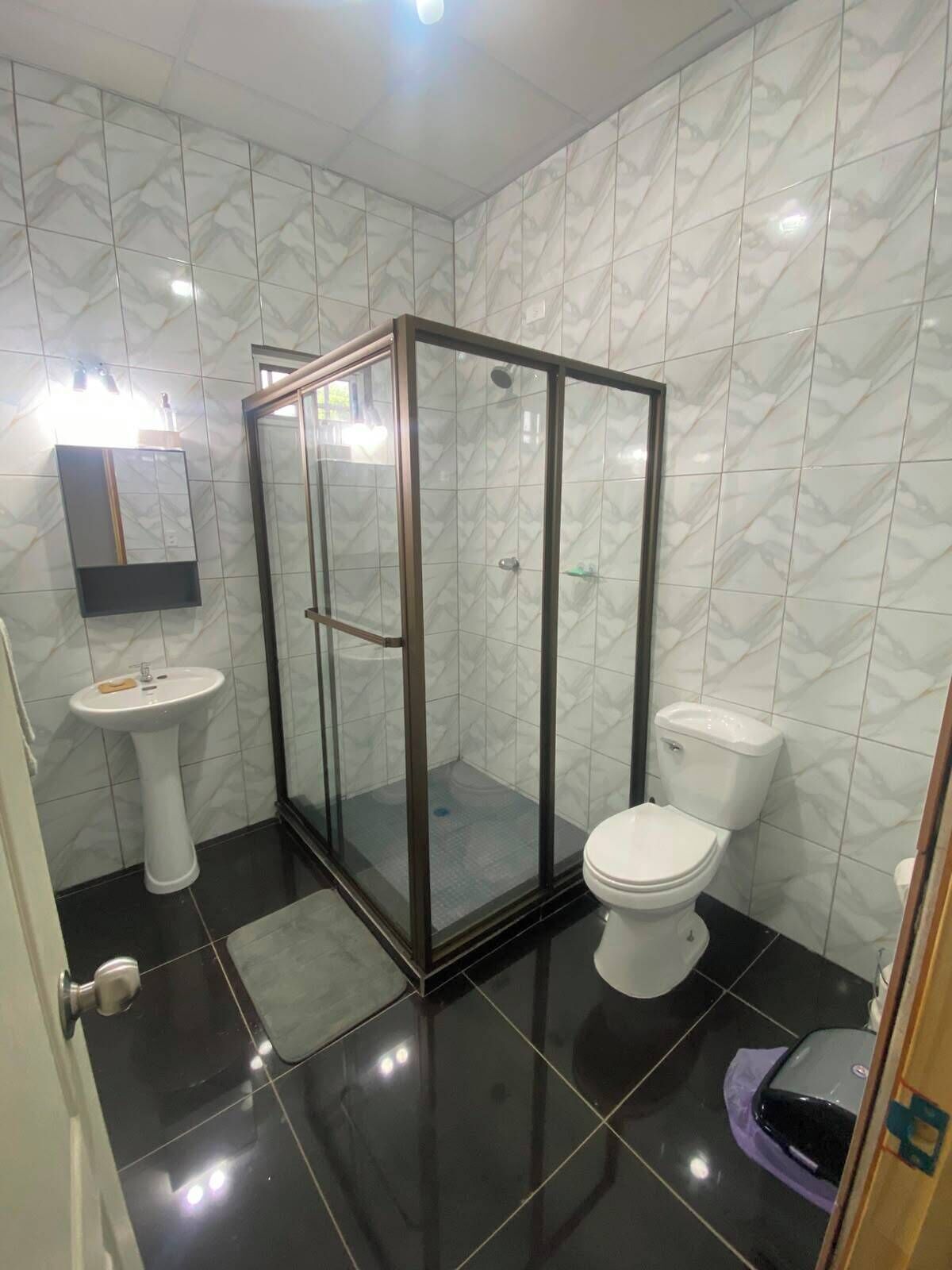 Een badkamer met een douchecabine van glas, een wit wastafeltje en een toilet.