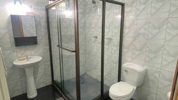 Een badkamer met een douchecabine van glas, een wit wastafeltje en een toilet.