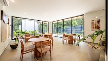 A spacious indoor area with large windows, wooden furniture, and potted plants.