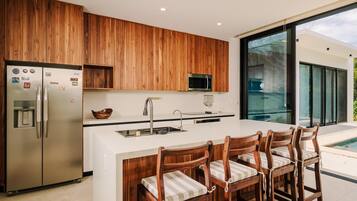 A modern kitchen with wooden cabinets, stainless steel appliances, a central island with bar stools, and a large window offering a view of the outdoors.