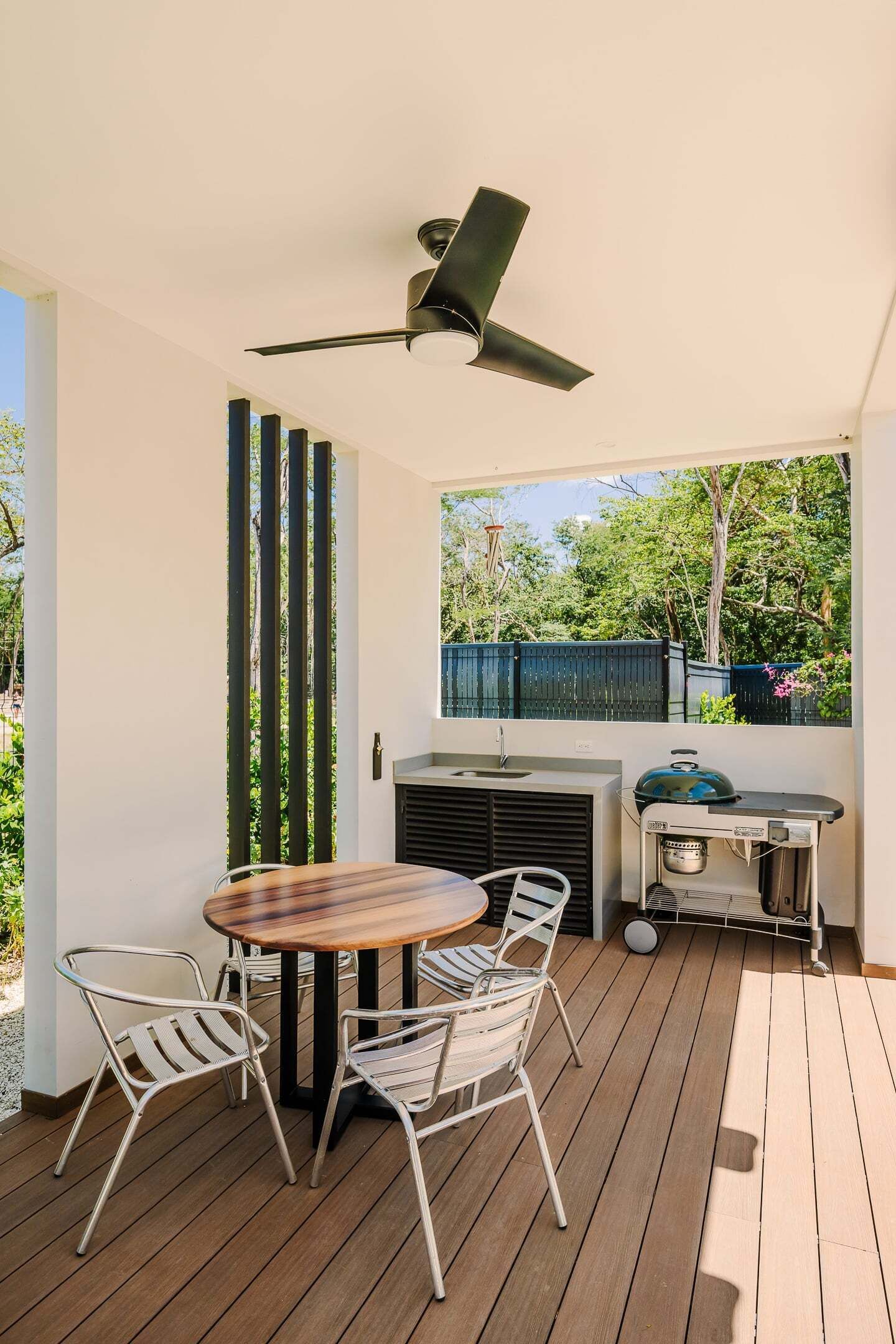 Una veranda esterna con un tavolo rotondo, sedie, una ventola a soffitto e un barbecue.