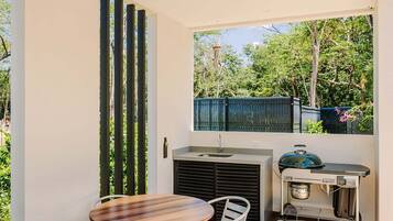 Una veranda esterna con un tavolo rotondo, sedie, una ventola a soffitto e un barbecue.
