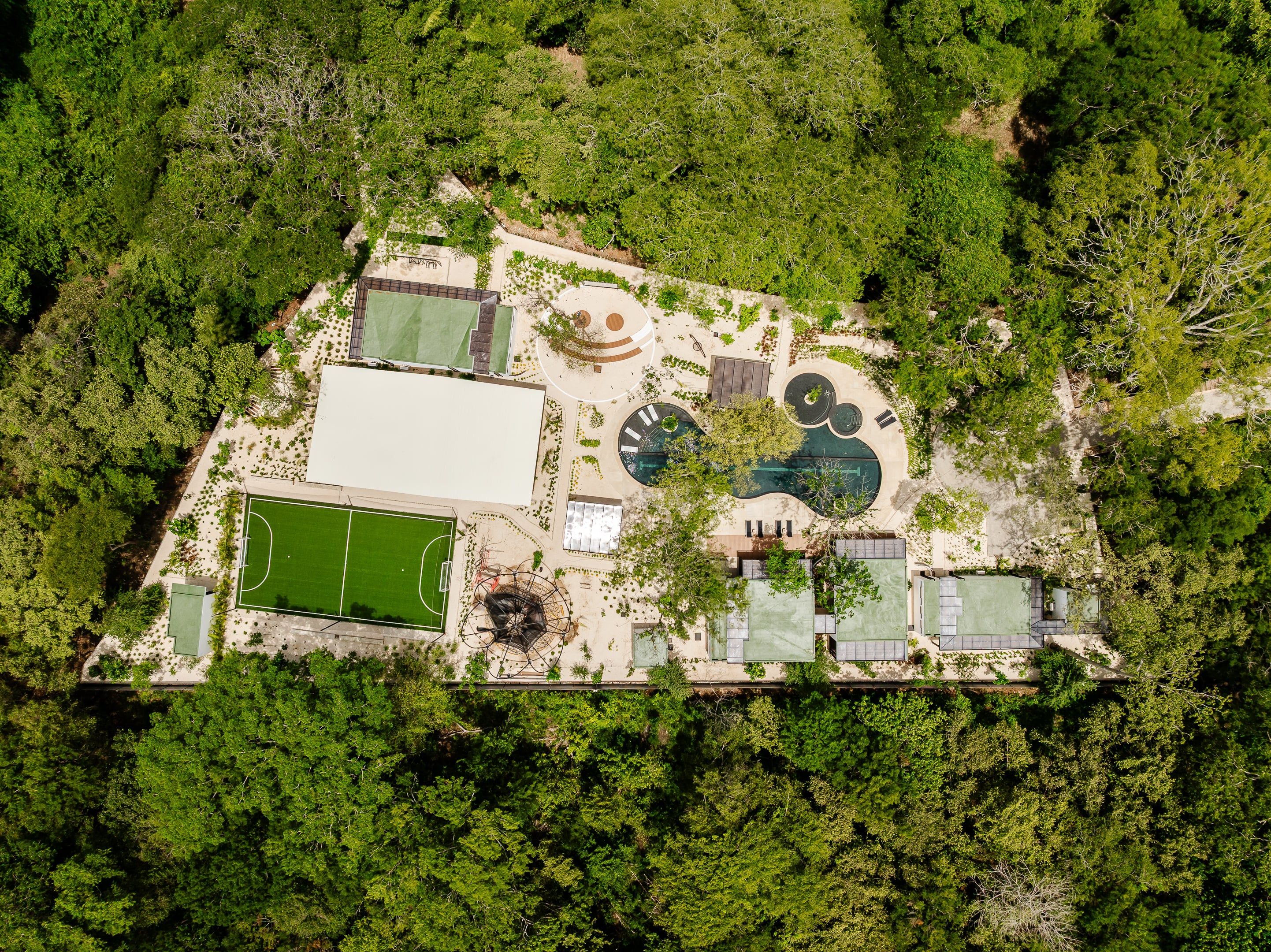 An aerial view of a property with a tennis court, a swimming pool, and a covered area.