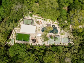 An aerial view of a property with a tennis court, a swimming pool, and a covered area.