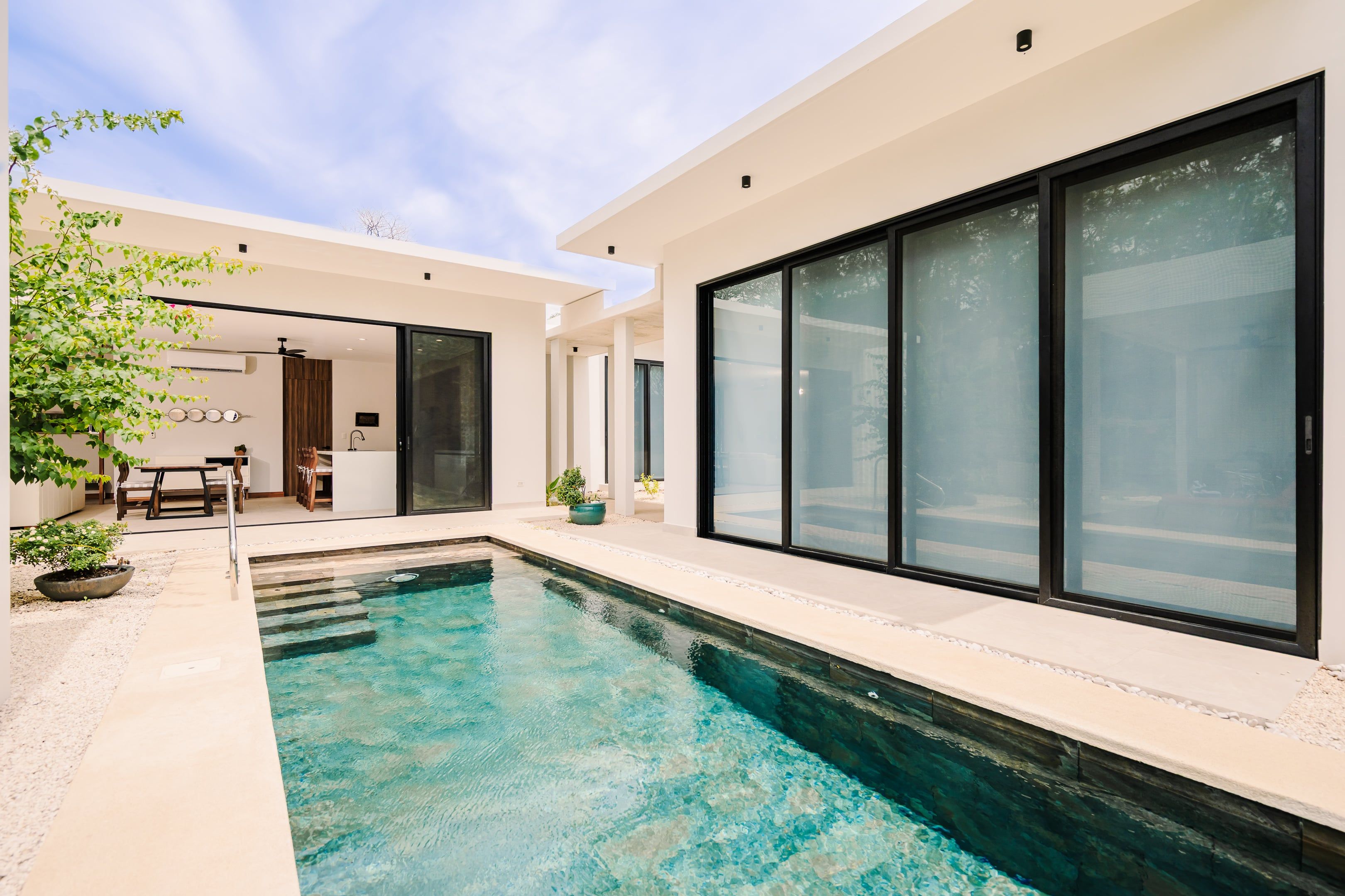 A modern outdoor swimming pool with clear water, surrounded by a patio area with seating and potted plants.