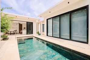 Piscina moderna ao ar livre, com água cristalina, cercada por um espaço de estar com assentos e vasos de plantas.