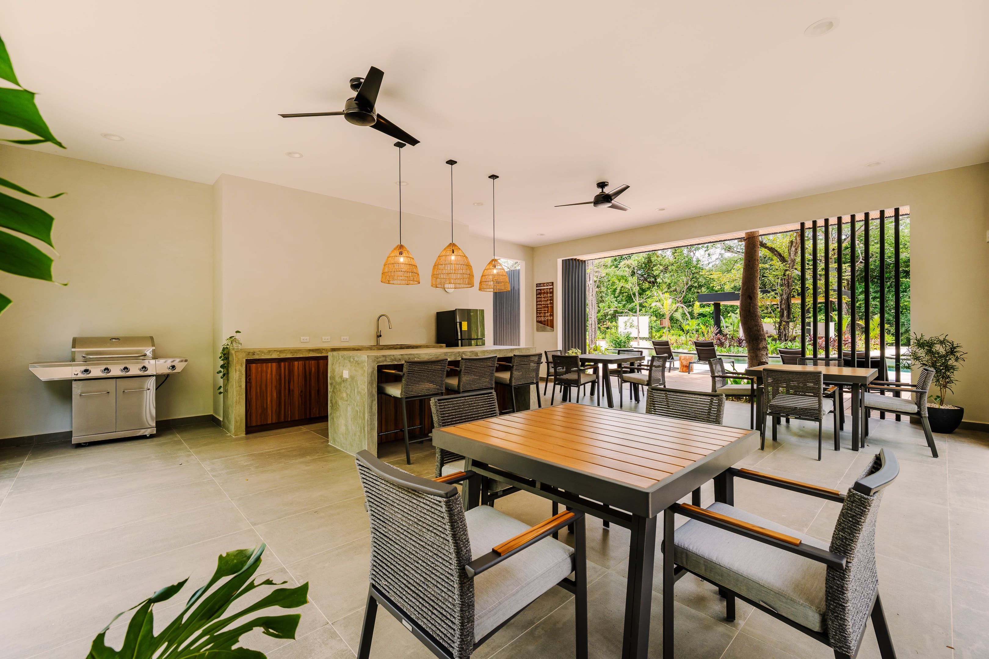 Un espacio moderno para comer al aire libre, con una parrilla, asientos y ventiladores de techo.