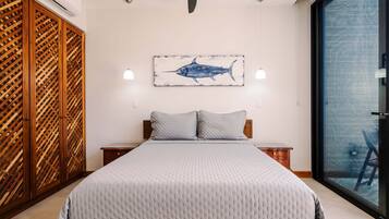 A bedroom with a bed, a wooden wardrobe, a wall-mounted artwork of a fish, bedside lamps, and a view through a glass door.