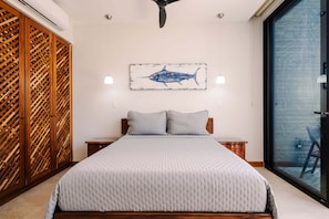 A bedroom with a bed, a wooden wardrobe, a wall-mounted artwork of a fish, bedside lamps, and a view through a glass door.