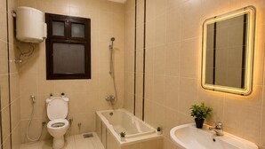Een badkamer met toilet, bad en wastafel, alles betegeld met beige tegels.