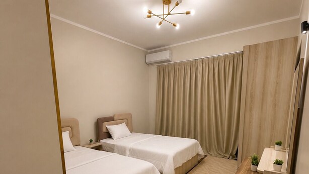 A hotel room with two beds, a wooden desk, a mirror, a small plant, and a ceiling light fixture.