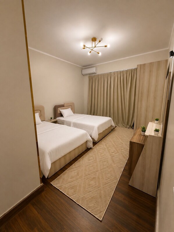 A hotel room with two beds, a wooden desk, a mirror, a small plant, and a ceiling light fixture. - Spacious 3-bedroom apartment in casa Beverly hills sodic Giza Governorate (Giza Governorate)