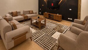 A modern living room with a sectional sofa, a coffee table, and a flat-screen TV mounted on a black wall.
