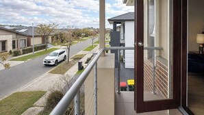 Un balcón con vistas a una calle residencial, un coche aparcado y un edificio de fachada blanca.