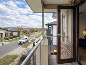 A balcony with a view of a residential street, a parked car, and a building with a white facade. - 4BR Point Cook Home | Sleeps 8 | Free Parking (Point Cook)