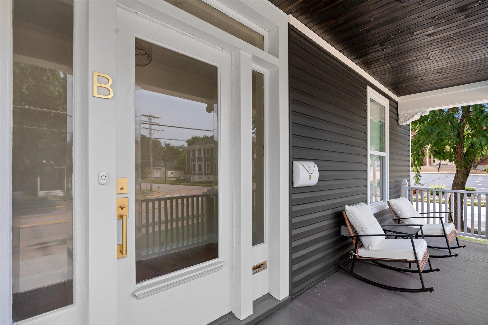 A hotel entrance with a white door, a mailbox, and a porch with two rocking chairs.