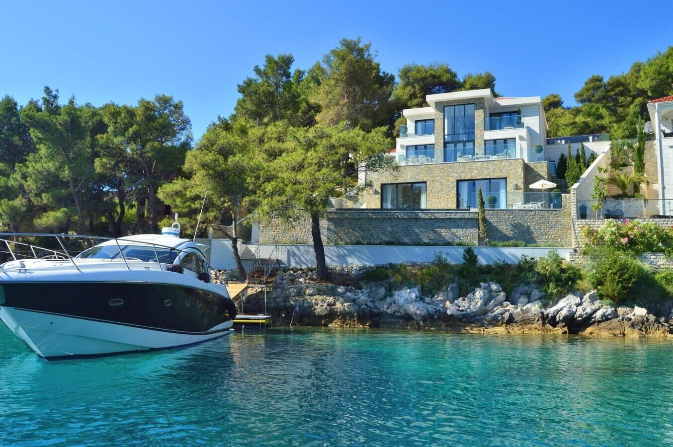 Une maison moderne avec une façade en pierre, une piscine et un bateau amarré au bord de l’eau.