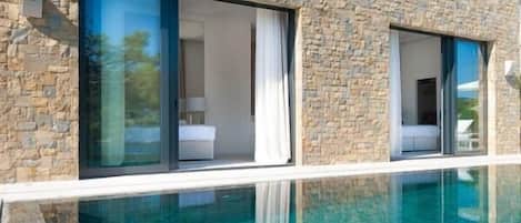 Un edificio moderno con fachada de piedra, grandes puertas correderas de cristal y una piscina azul cristalina.