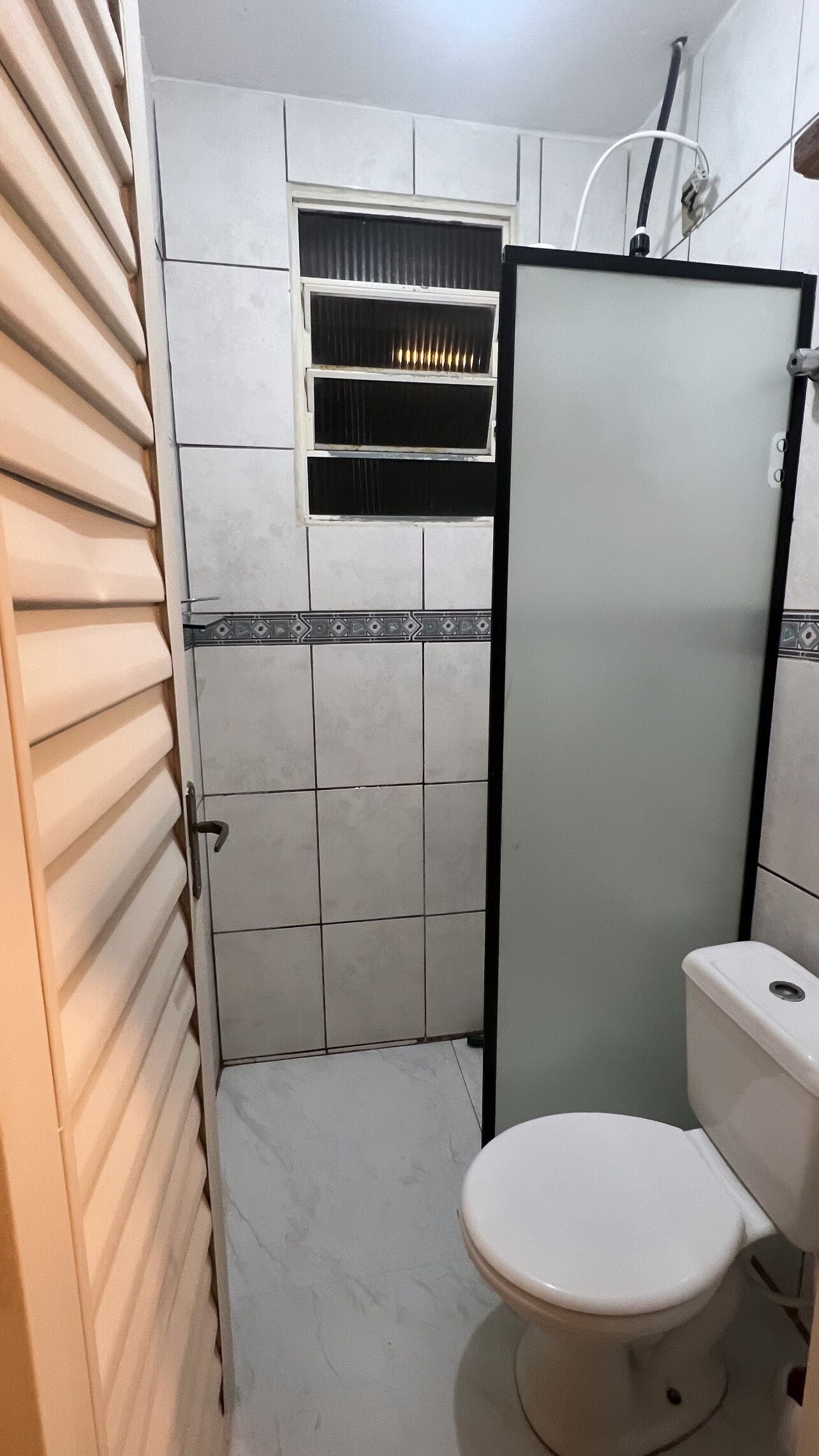 Un baño con inodoro, cabina de ducha y ventana con persianas.