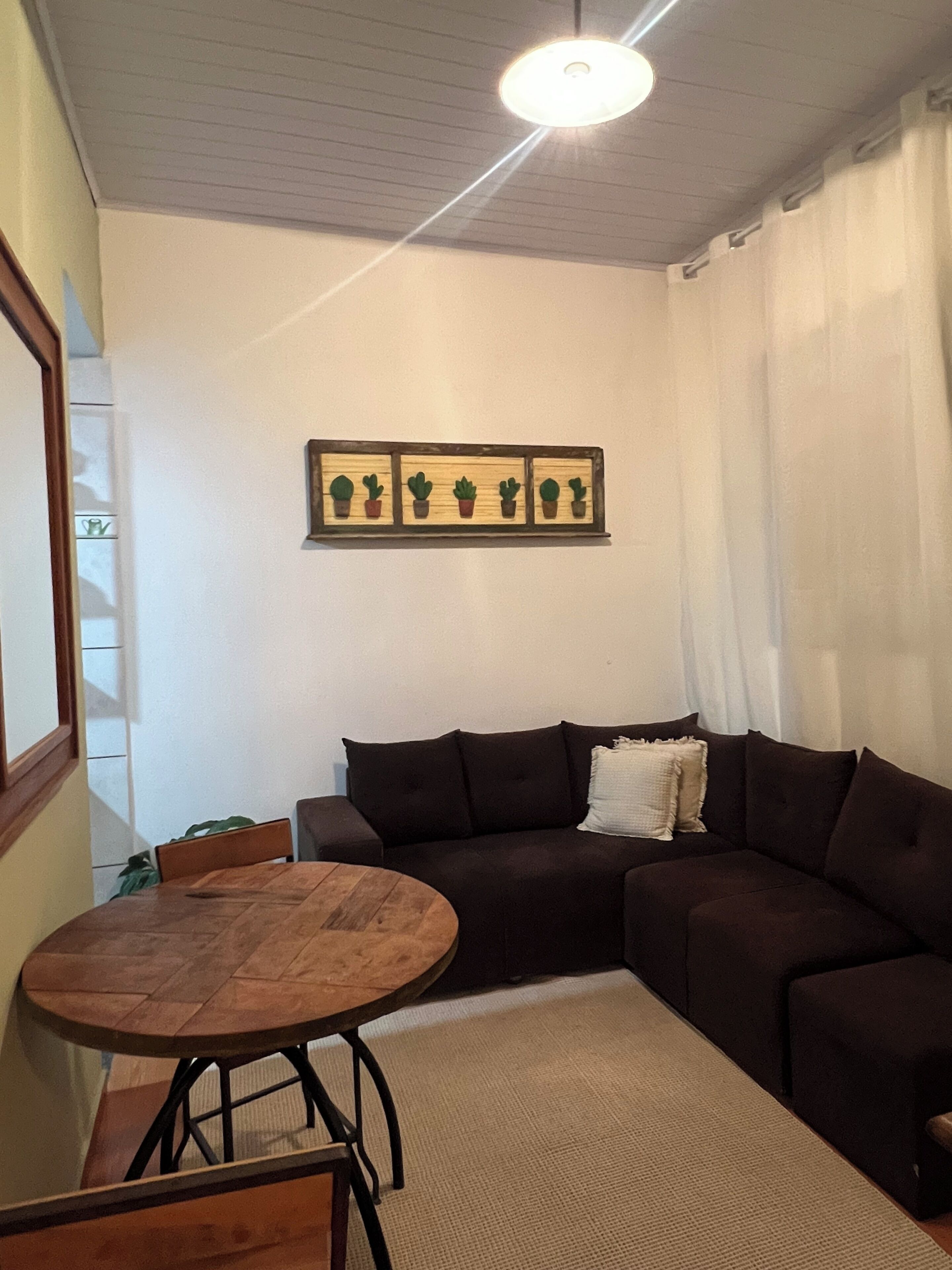 Sala de estar com um sofá marrom escuro, uma mesa de madeira redonda e um lustre no teto.