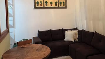 Un salon avec un canapé marron foncé, une table ronde en bois et un luminaire suspendu au plafond.