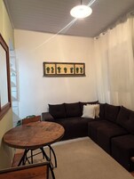 Una sala de estar con un sofá marrón oscuro, una mesa redonda de madera y una lámpara en el techo.