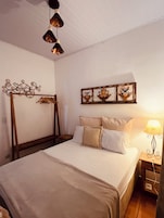 Un dormitorio con cama, mesita de noche, lámpara, decoración en la pared y un perchero de madera.
