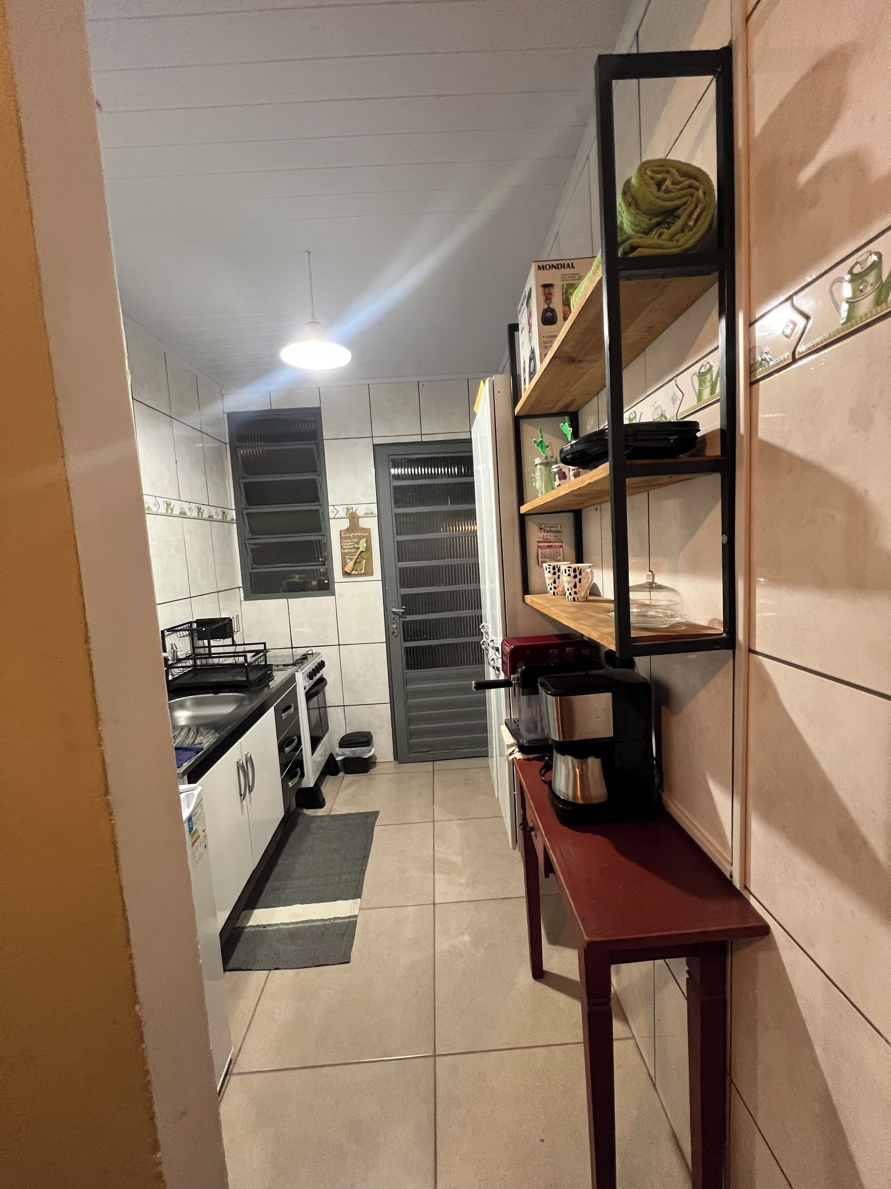 Een smalle keuken met witte kasten, een fornuis en een koffiezetapparaat op een houten tafel.