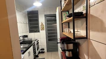 Een smalle keuken met witte kasten, een fornuis en een koffiezetapparaat op een houten tafel.