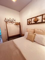 A bedroom with a bed, a wooden headboard, a wall-mounted art piece, and a hanging light fixture.