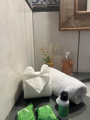 Une salle de bain avec une serviette, un flacon de savon liquide et un petit sachet vert posé sur le comptoir.