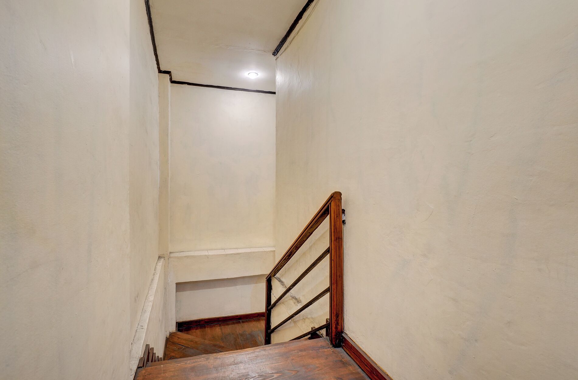 A narrow stairway with wooden handrails and a white wall.