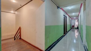 A long, narrow hallway with a wooden staircase on the left, a green and white wall on the right, and a tiled floor.