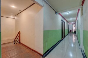 A long, narrow hallway with a wooden staircase on the left, a green and white wall on the right, and a tiled floor.