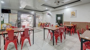 A restaurant interior with red chairs and tables, a ceiling fan, and a view of the street through the open door.