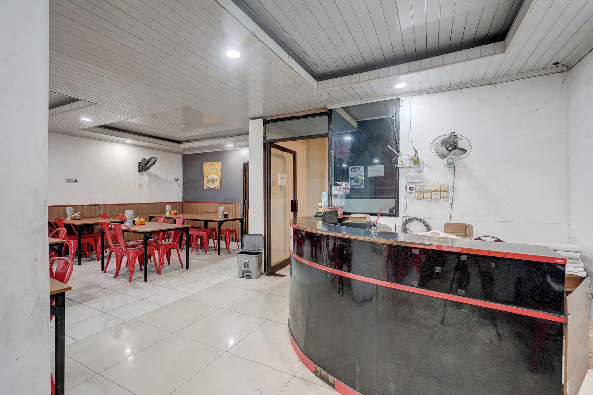 Interior de restaurante com balcão, cadeiras vermelhas e piso de azulejos.