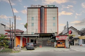 Un hotel con un letrero llamativo, un coche estacionado y un pequeño quiosco.