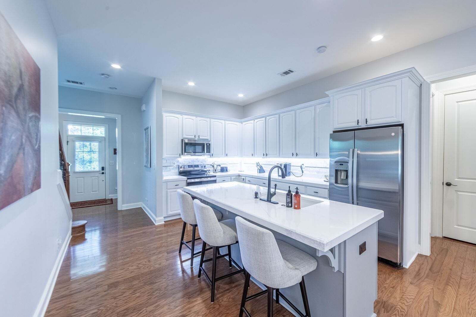 A modern kitchen with white cabinetry, stainless steel appliances, and a central island with bar stools.