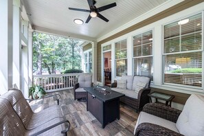Eine überdachte Veranda mit Deckenventilator, Sitzgelegenheiten im Freien und großen Fenstern.